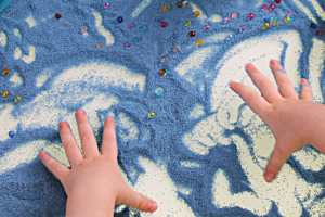 A young child is playing with with blue sand.